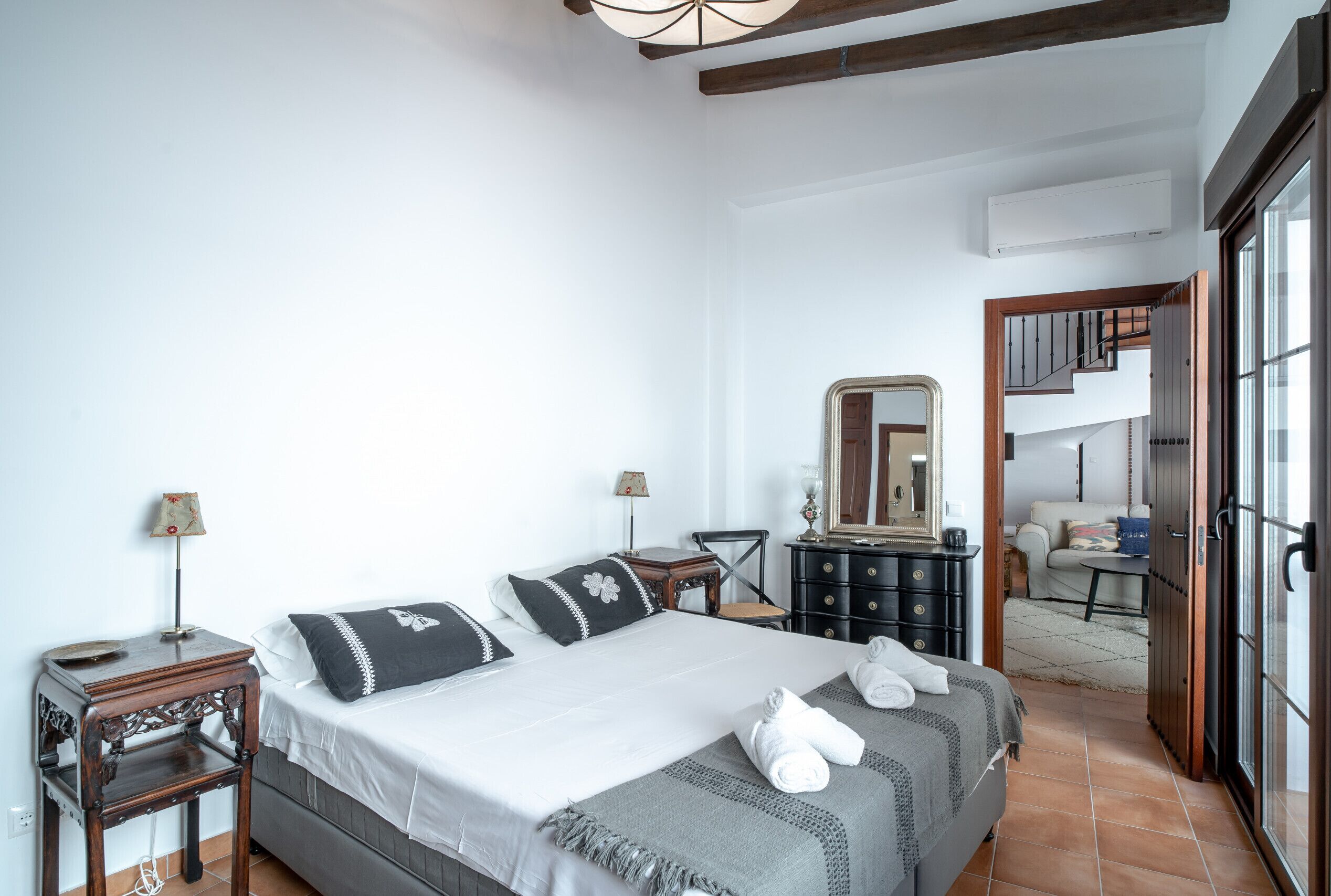 Ein Schlafzimmer mit einem großen Bett, zwei Nachttischen, einer Kommode, einem Spiegel und einer Treppe zu einer oberen Etage.