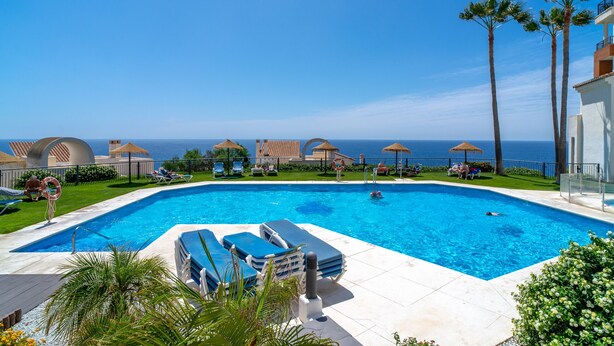 A swimming pool with lounge chairs and umbrellas, a view of the sea, and a building with a balcony. - Calaceite 5101 Ocean Paradise by Casasol (Torrox)