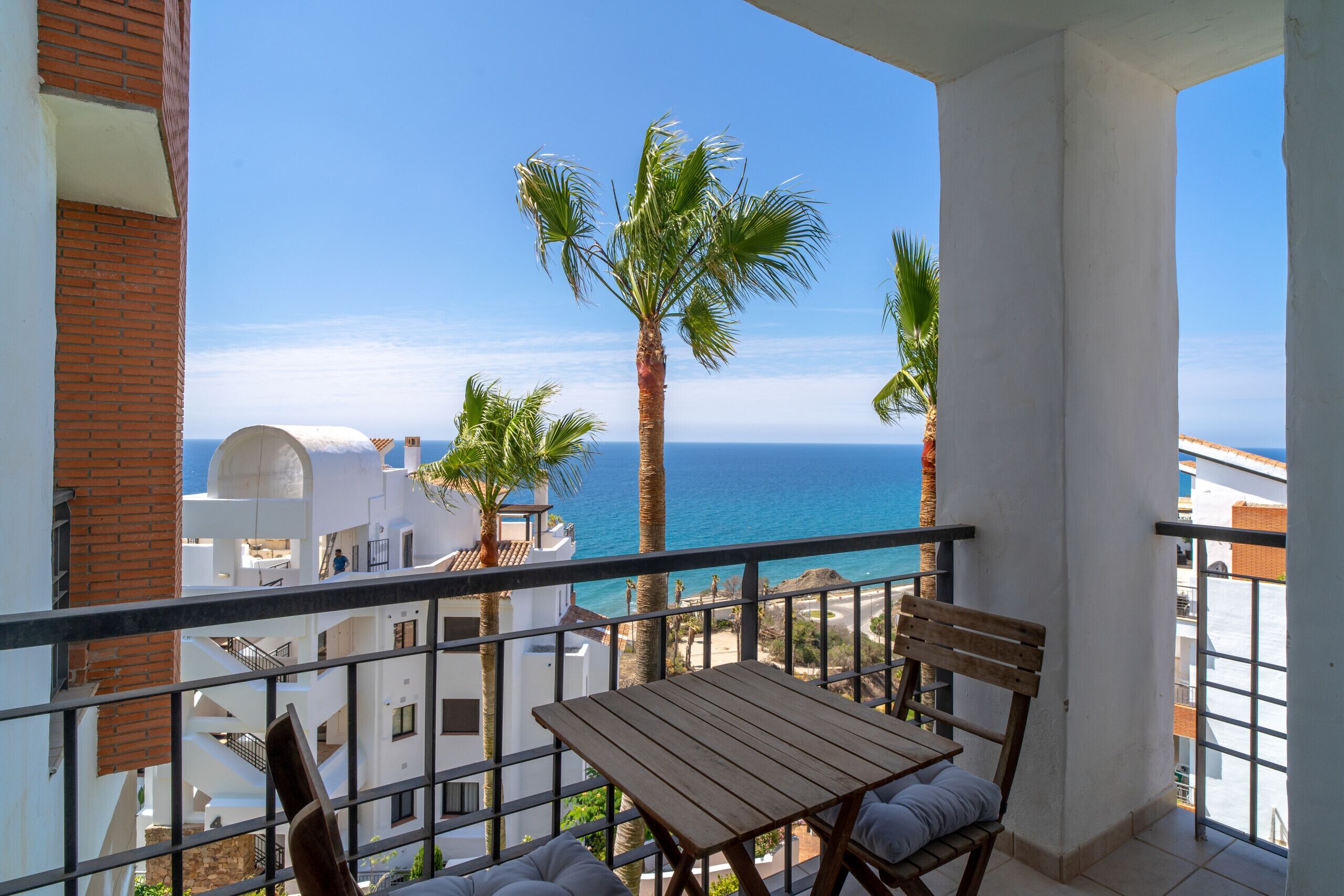 A balcony with a table and chairs, overlooking a beach and palm trees.