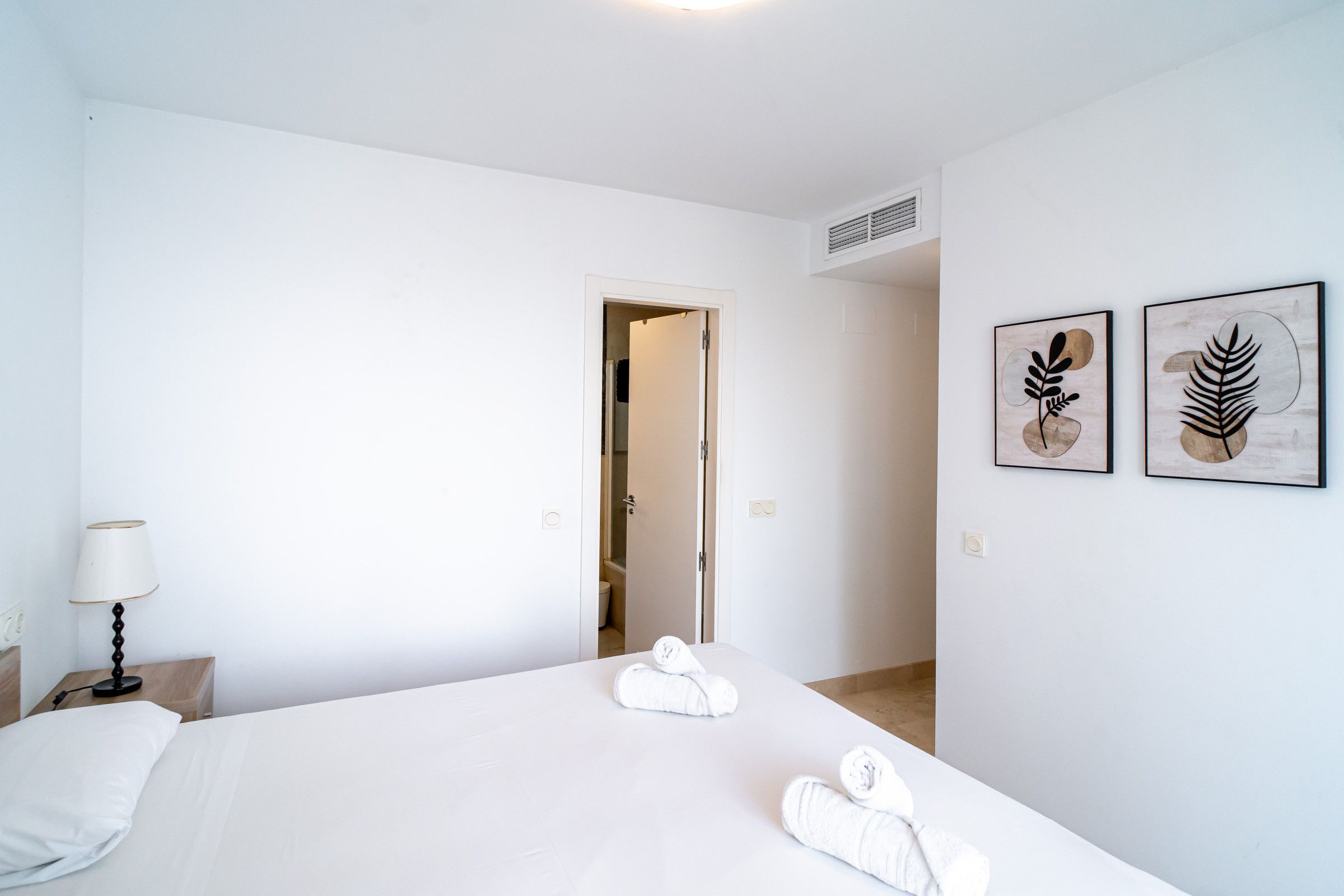 A hotel room with a bed, a nightstand, a lamp, and two wall art pieces.