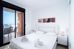 A hotel room with a bed, a nightstand, a lamp, a painting, and a view of the outdoors through a sliding door. - Calaceite 5101 Ocean Paradise by Casasol (Torrox)