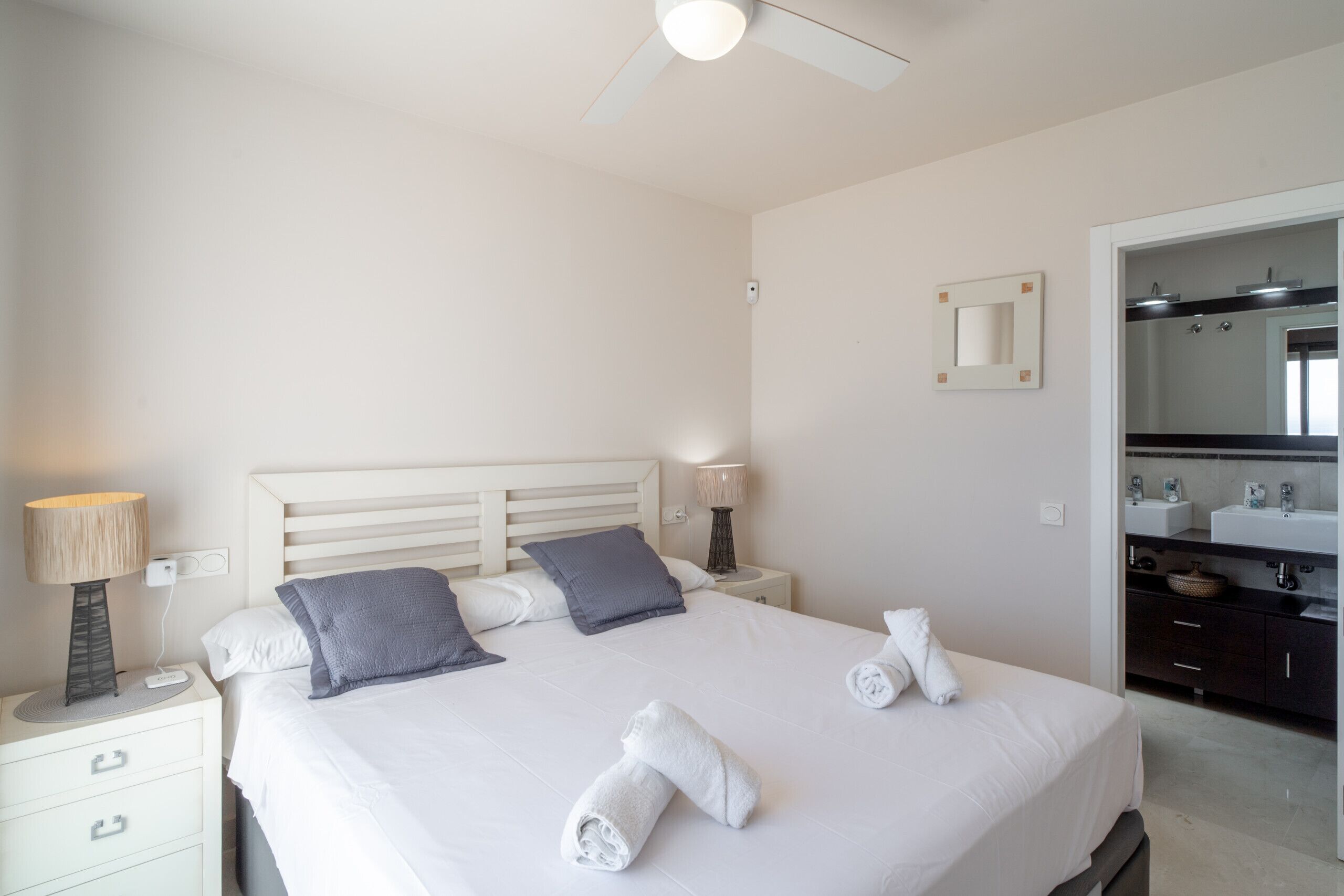 A hotel room with a bed, bedside lamps, a nightstand, a mirror, and a bathroom with a sink and mirror.