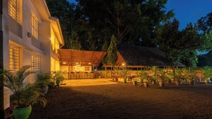 A building with a covered patio area, potted plants, and a dirt ground.