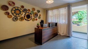 A reception desk with a laptop, a potted plant, and a wall decorated with woven plates.