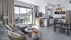 Eine moderne Wohnung mit Wohnzimmer, Essbereich, Küche und großen Schiebegläsern, die auf einen Balkon mit Bergblick führen.