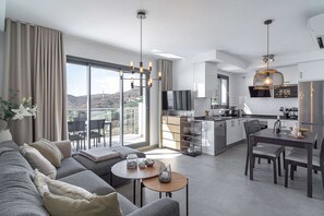 Eine moderne Wohnung mit Wohnzimmer, Essbereich, Küche und großen Schiebegläsern, die auf einen Balkon mit Bergblick führen.