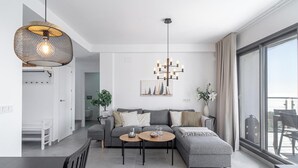 Ein modernes Wohnzimmer mit grauem Sofa, einem Couchtisch und einer Chandelier. Es gibt einen Essbereich mit Tisch und Stühlen, und ein großes Fenster mit Blick.