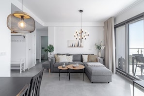 Ein modernes Wohnzimmer mit grauem Sofa, einem Couchtisch und einer Chandelier. Es gibt einen Essbereich mit Tisch und Stühlen, und ein großes Fenster mit Blick.