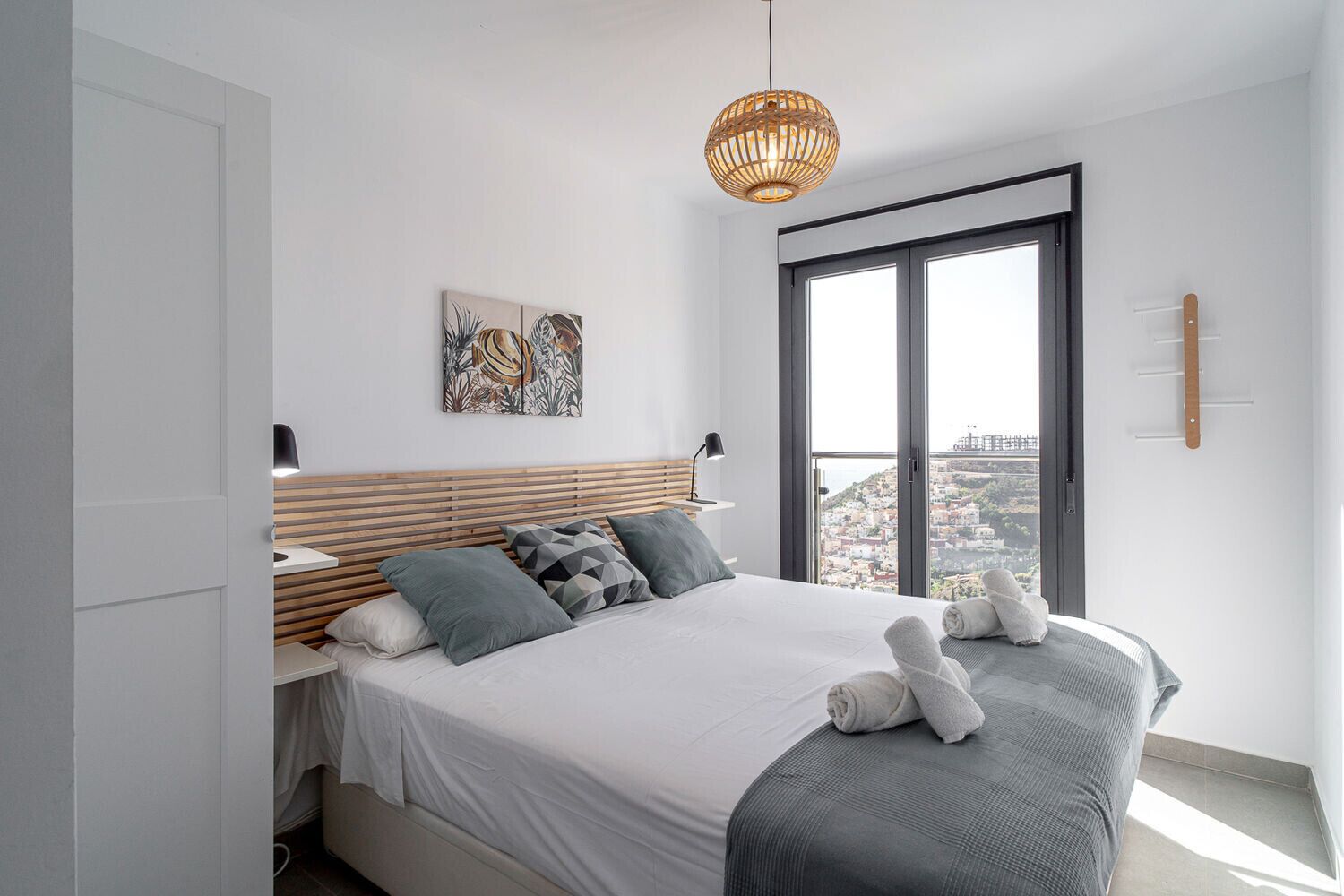 Un dormitorio moderno con una cama grande, vistas a la ciudad a través de la ventana y una lámpara colgante.