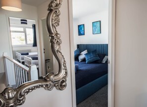 A bedroom with a bed, a mirror, and two framed artworks on the wall. - Sea Breeze Beach House (Seaford)