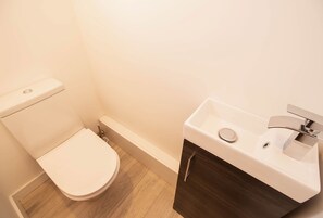 A bathroom with a toilet, a sink, and a wooden floor. - Sea Breeze Beach House (Seaford)