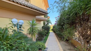 A narrow paved pathway flanked by lush greenery and a building with a tiled roof. - Senorio de Capistrano by Casasol (Nerja)