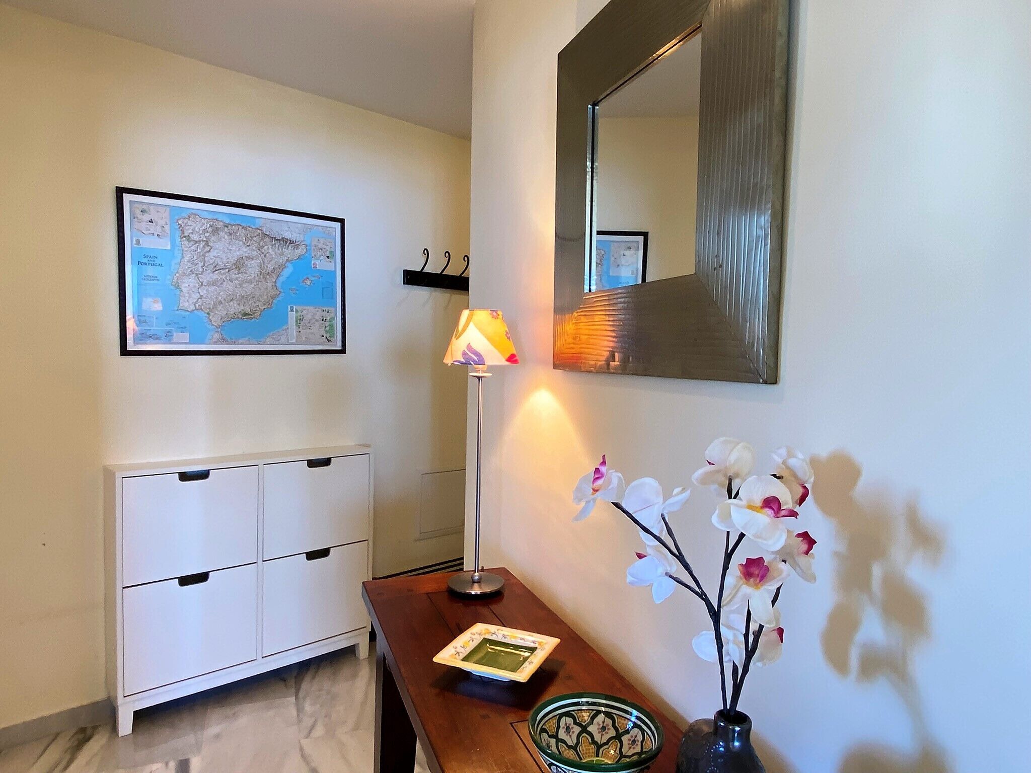 Een kamer met een kaart aan de muur, een bureau met een lamp, een spiegel en een vaas met orchideeën.