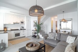 Eine moderne Küche mit weißen Schränken, ein Essbereich mit grauem Sofa und eine Treppe, die zu einer oberen Ebene führt.