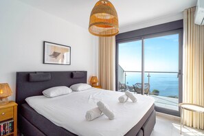 Ein modernes Hotelzimmer mit einem großen Bett, Blick auf das Meer, einer Korbtrophäe und einem gerahmten Bild an der Wand.