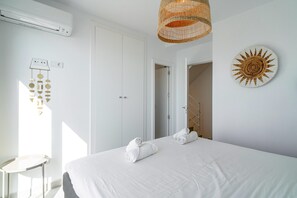 Ein Schlafzimmer mit einem Bett, einem Nachttisch, einer Wandklimaanlage, einer gewebten Leuchte und einem Wandbild.
