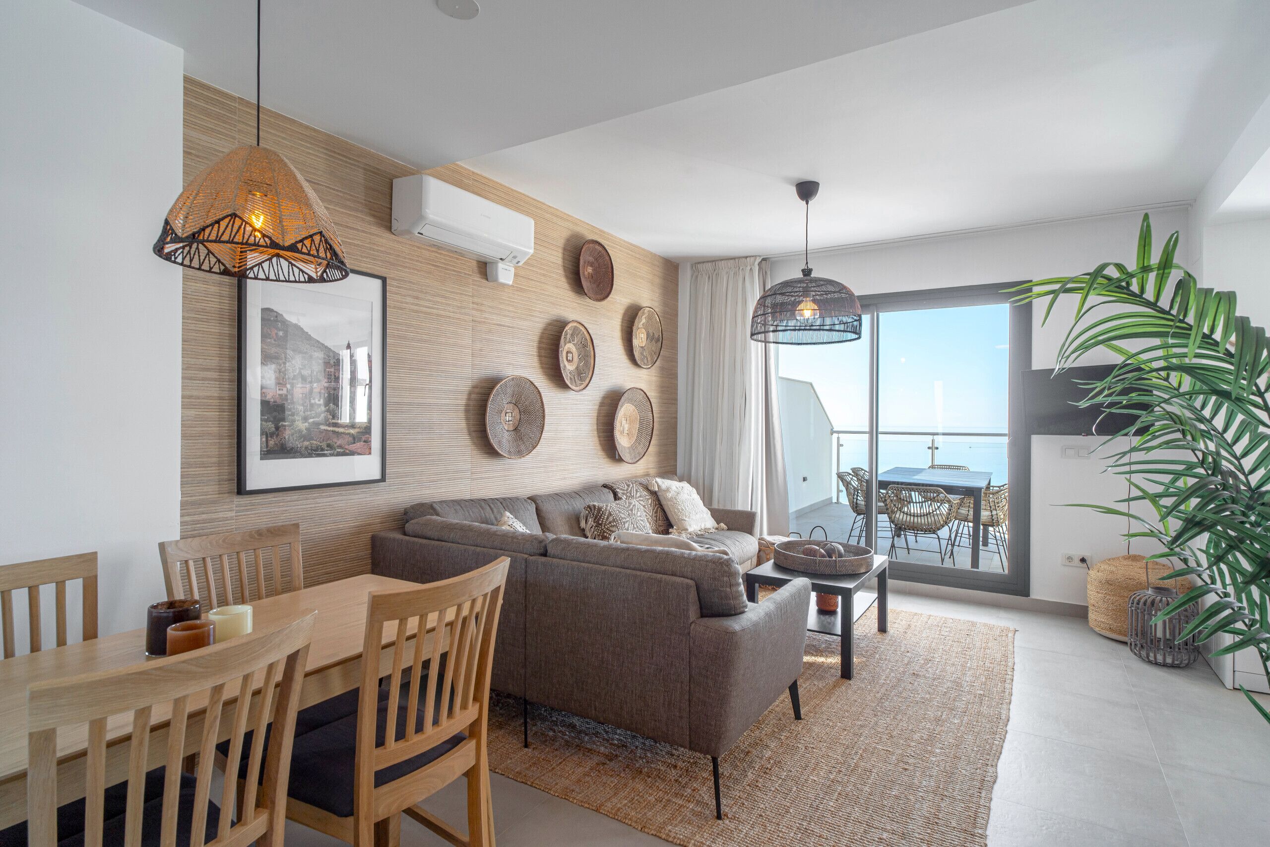 A modern living room with a sofa, dining table, and chairs, a large window with a view, and decorative wall art.