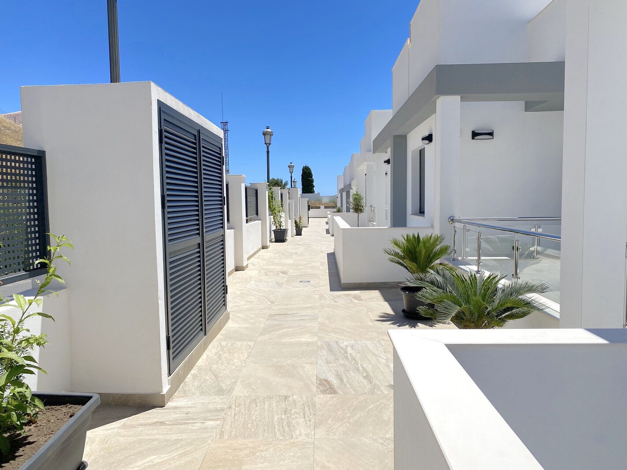 A modern residential building with a clean, minimalist design, featuring a tiled walkway and potted plants.