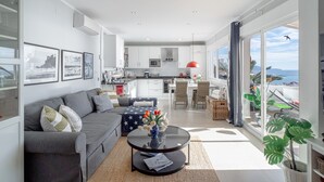 A modern living room with a gray sofa, a coffee table with a vase of flowers, and a view of the kitchen and balcony. - Vistas del Mar by Casasol (Nerja)