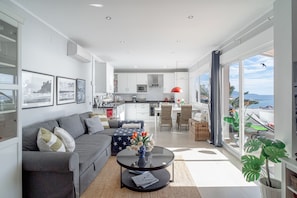 A modern living room with a gray sofa, a coffee table with a vase of flowers, and a view of the kitchen and balcony. - Vistas del Mar by Casasol (Nerja)