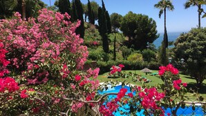 A pool area with a view of the sea, surrounded by lush greenery and tall trees. - Vistas del Mar by Casasol (Nerja)