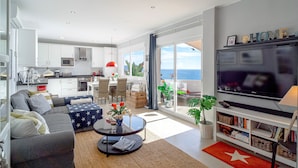 A modern living room with a sofa, coffee table, and TV. There is a balcony with a view of the ocean. - Vistas del Mar by Casasol (Nerja)