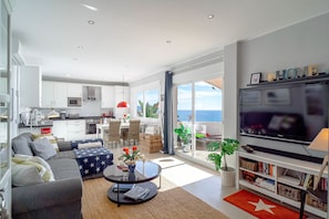 A modern living room with a sofa, coffee table, and TV. There is a balcony with a view of the ocean. - Vistas del Mar by Casasol (Nerja)