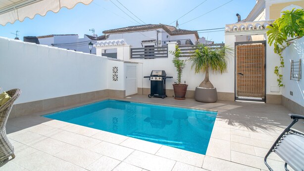 Ein Swimmingpool mit Fliesenveranda, Grill und Topfpflanzen.