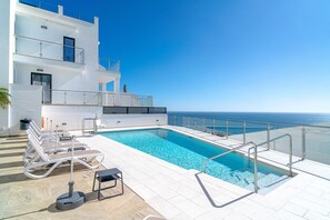Ein moderner Poolbereich mit Liegestühlen und freiem Blick auf das Meer.