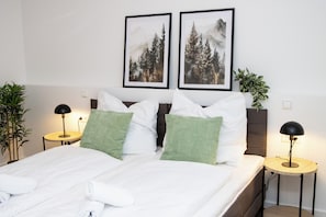 A neatly made bed with white linens, two framed pictures on the wall, and two bedside tables with lamps. - Apartment 2: Modern, Terrace, Near Europa Park & A5 (Appenweier)