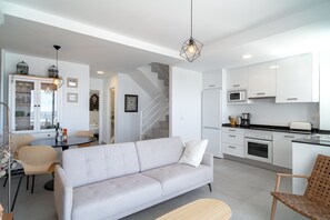 Eine moderne Küche mit weißen Schränken, einer Mikrowelle und einem Toaster. Es gibt einen Essbereich mit Tisch und Stühlen sowie ein Sofa im Wohnzimmer.