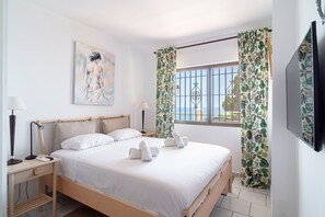 Ein Schlafzimmer mit Bett, Nachttischen, einer Lampe, einem Gemälde und Vorhängen.