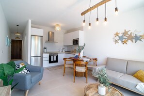 Ein modernes Wohnzimmer mit einer Couch, einem Esstisch mit Stühlen und einer Küchenzeile mit Kühlschrank und Mikrowelle.
