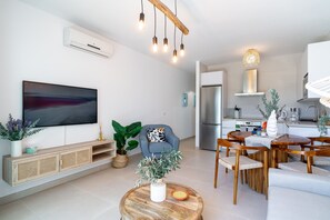 Ein modernes Wohnzimmer mit Flachbildfernseher, Holzmöbeln und einem Essbereich mit Tisch und Stühlen.