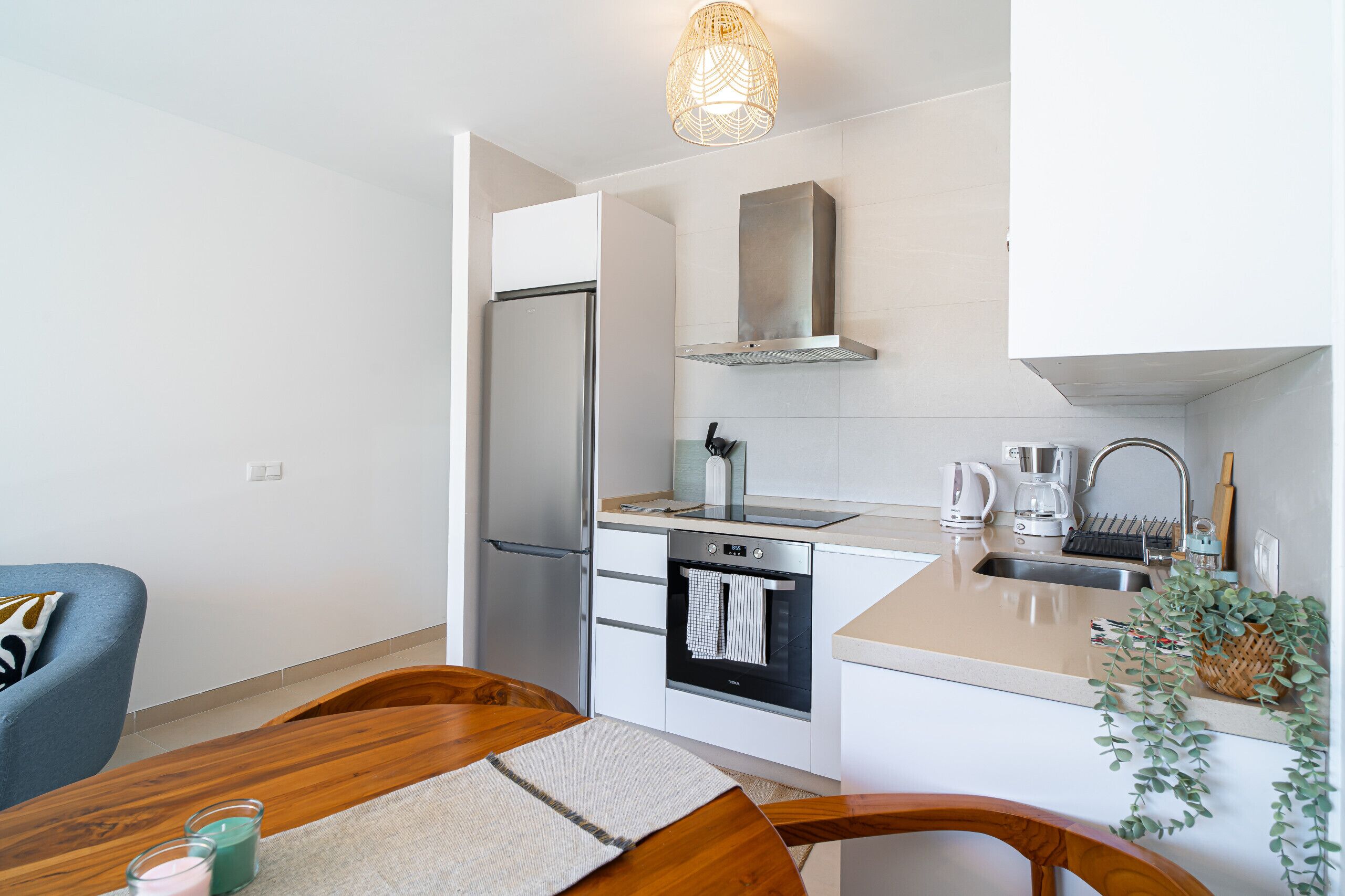 Cocina compacta con refrigerador, horno y lavamanos. Hay una mesa de comedor con sillas y una lámpara colgante.