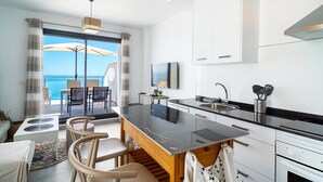 A modern kitchen with a large island, a dining area with chairs, a view of the ocean, and a ceiling fan. - Terrazas de Ladera A2 Luxury by Casasol (Nerja)