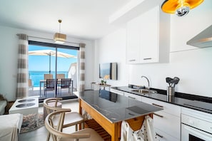 Eine moderne Küche mit einer großen Kochinsel, einem Essbereich mit Stühlen, Blick aufs Meer und einem Deckenventilator.