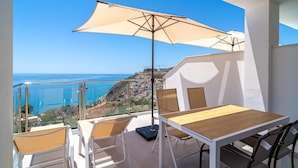 A balcony with a table and chairs, a large umbrella, and a view of the coastline. - Terrazas de Ladera A2 Luxury by Casasol (Nerja)