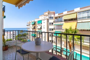 Ein Balkon mit Tisch und Stühlen, mit Blick auf einen Pool und Gebäude mit Balkonen.
