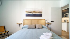 A neatly made bed with a light blue bedspread and two pillows, a wicker headboard, and a painting of a landscape above the bed. - Albaida Seaview by Casasol (Nerja)