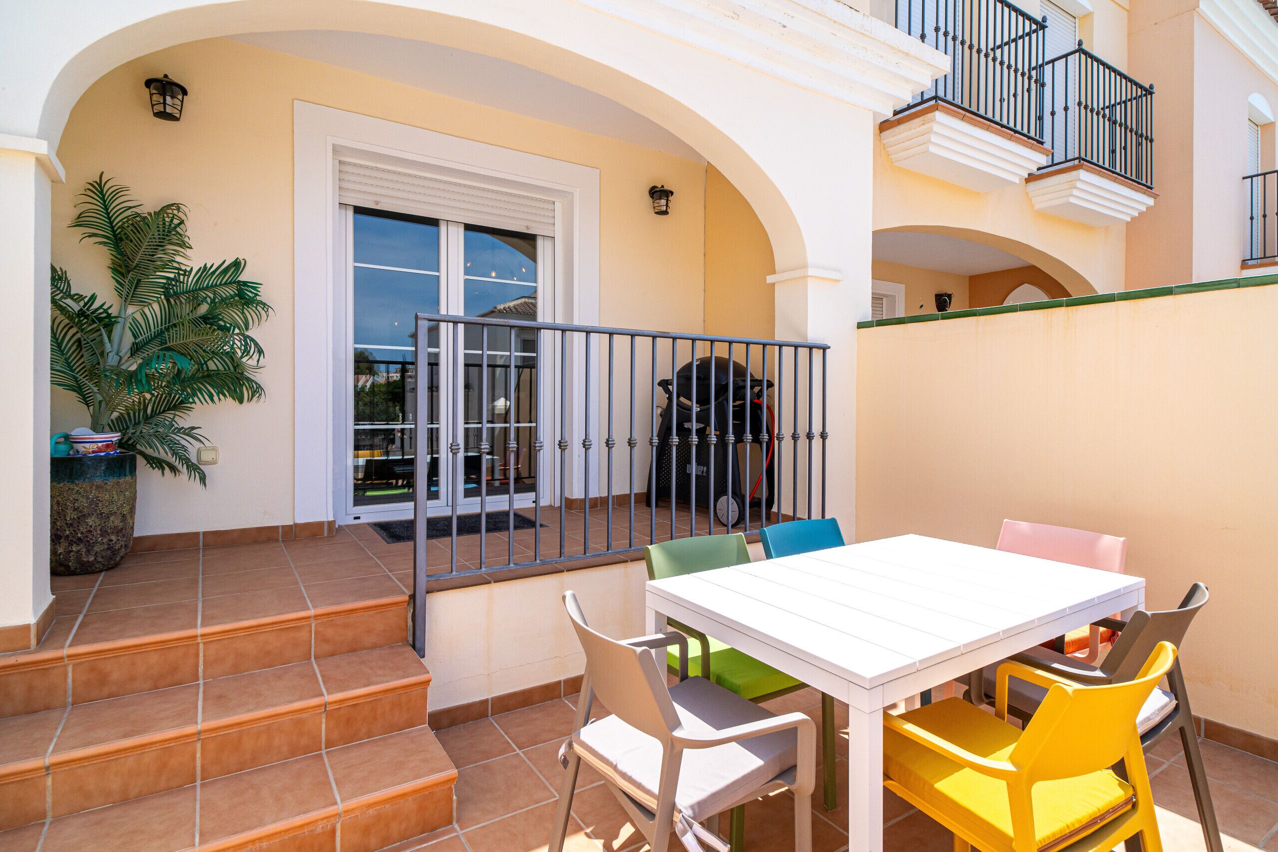 Un patio con una mesa y sillas blancas, una planta en maceta y una escalera que lleva a una puerta.