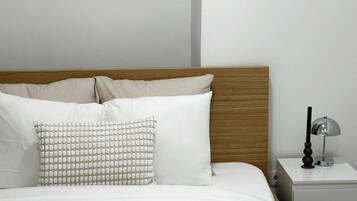 Un letto rifatto con cura, lenzuola bianche, un cuscino decorato e un asciugamano piegato.