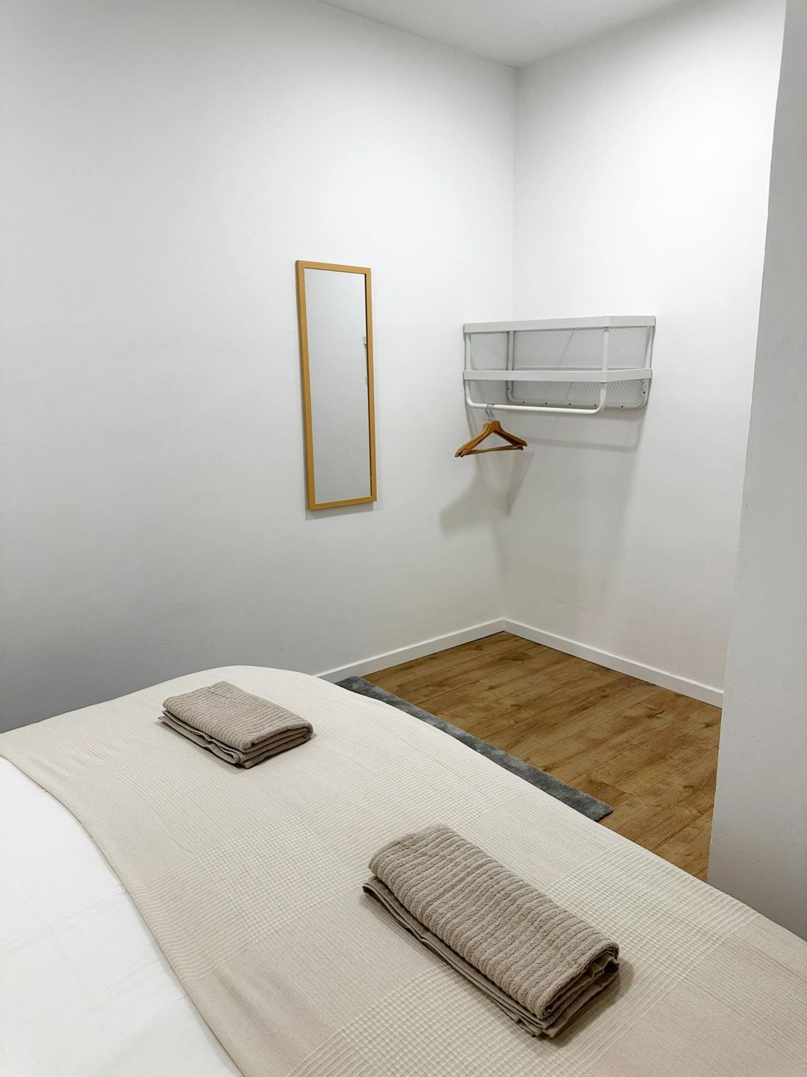 Una habitación pequeña y limpia con una cama, un perchero de madera y un estante blanco.