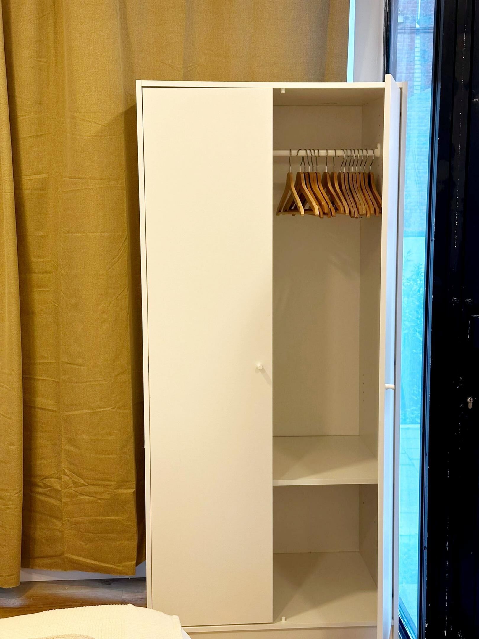 Un armario blanco con perchas de madera, una puerta blanca y una ventana con vista a edificios.