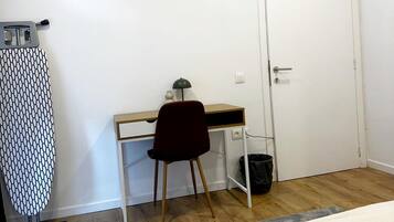 A bedroom with a bed, a desk, a chair, a door, and an ironing board.