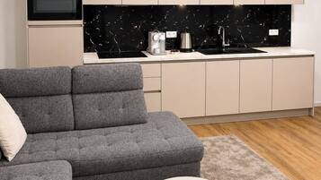 A modern living room with a grey sectional sofa, a round coffee table, and a kitchen area with a black marble backsplash.