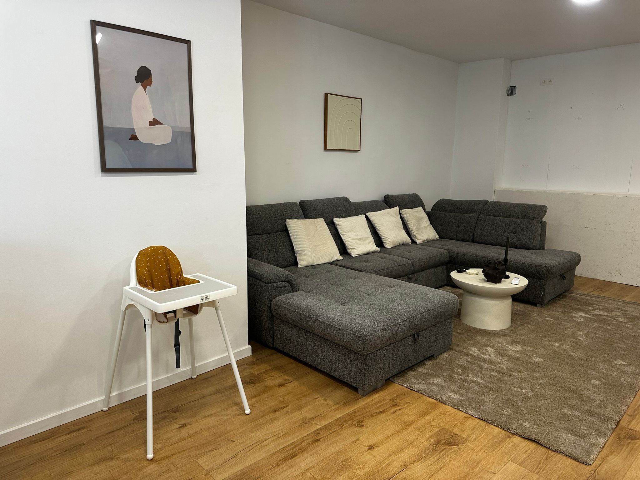 A modern living room with a grey sectional sofa, a white side table, a small white chair, and a framed picture on the wall.