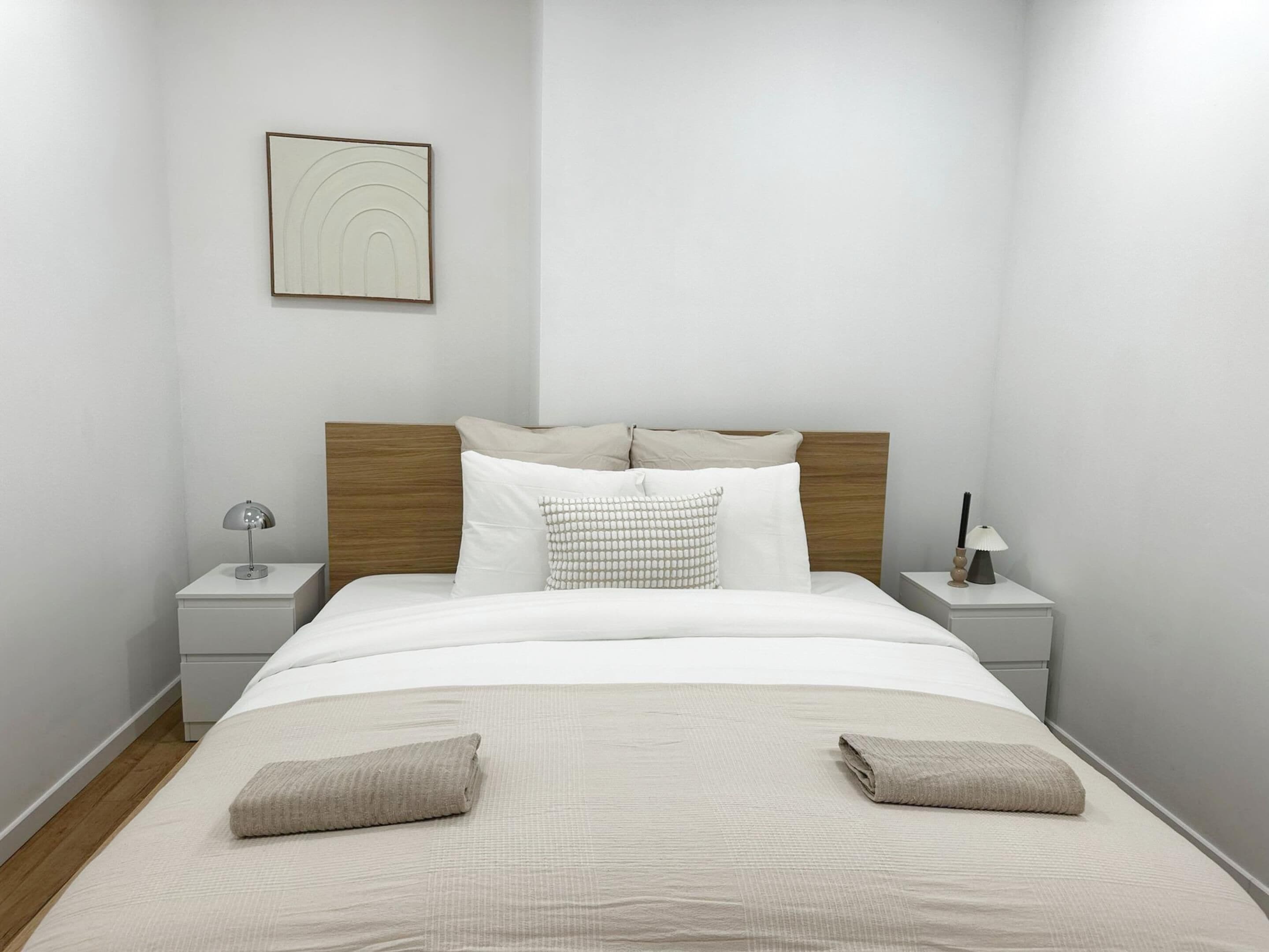 Un lit bien fait, avec une tête de lit en bois, deux tables de chevet avec des lampes et une œuvre d’art accrochée au mur.
