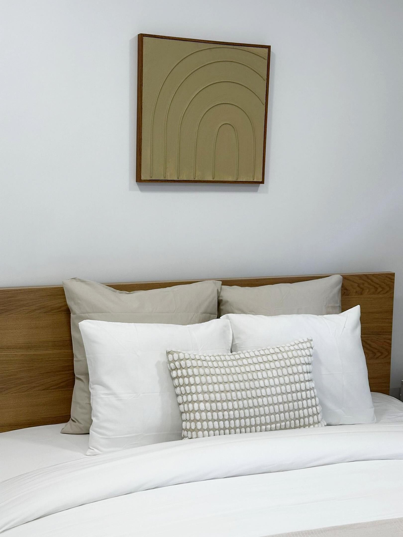Una cama con cabecera de madera, dos almohadas y una obra de arte colgada en la pared.