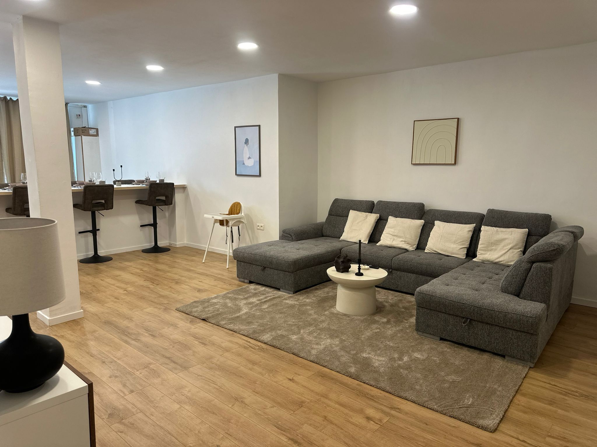 Una sala de estar moderna con un sofá seccional gris, una mesita redonda y suelo de madera.
